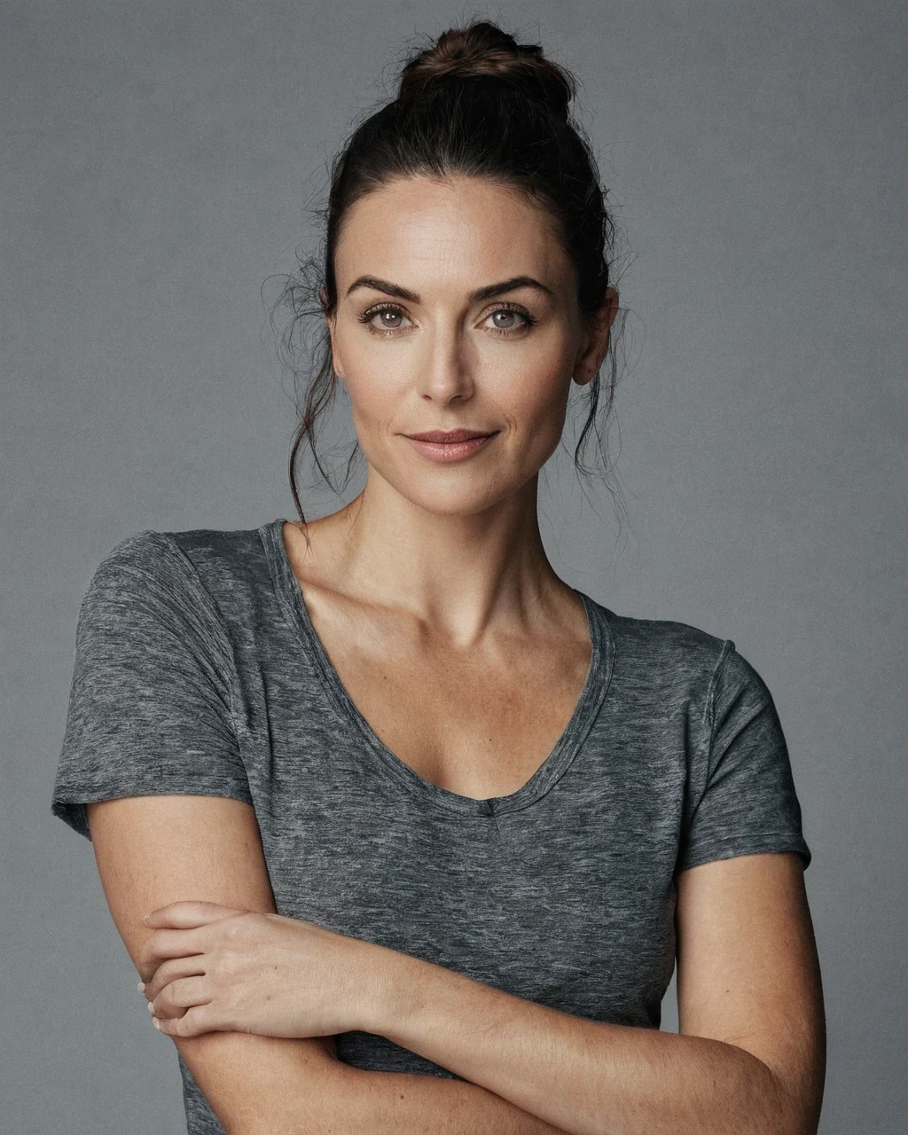 An adult woman in a grey t-shirt, arms crossed, on a plain grey studio backdrop