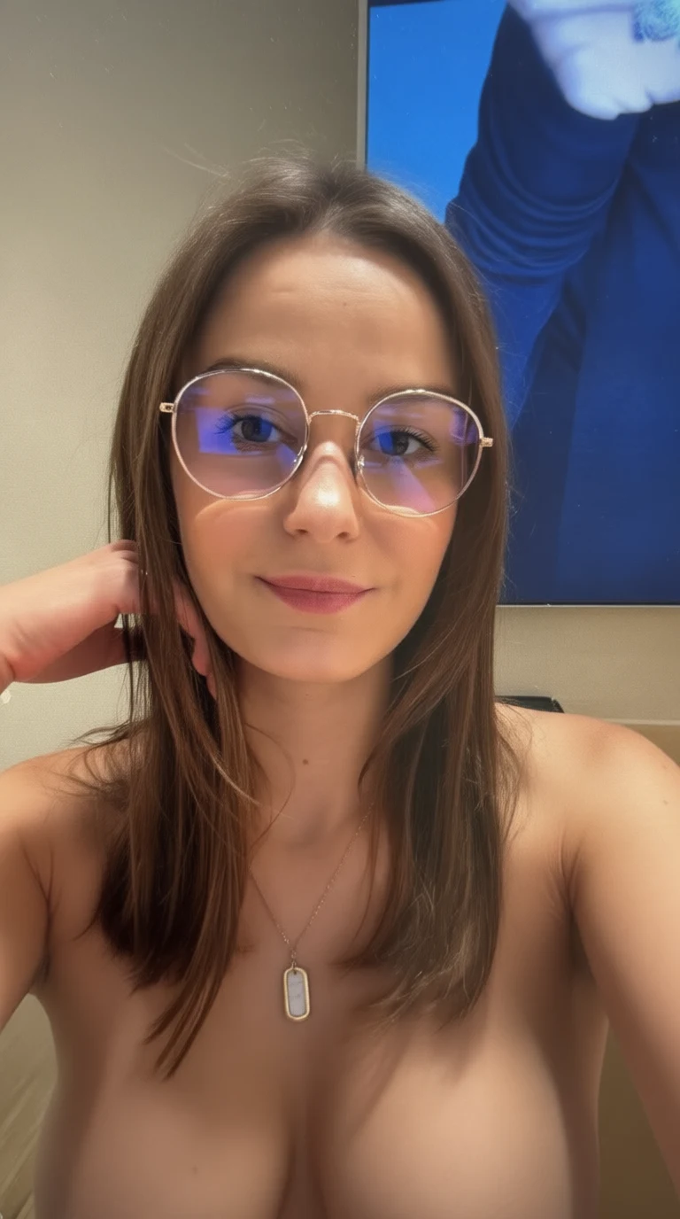 A woman with brown hair and round glasses smiles while touching her hair