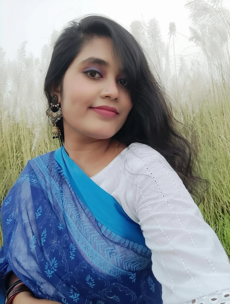 A woman in a blue patterned sari and white blouse smiles in a field